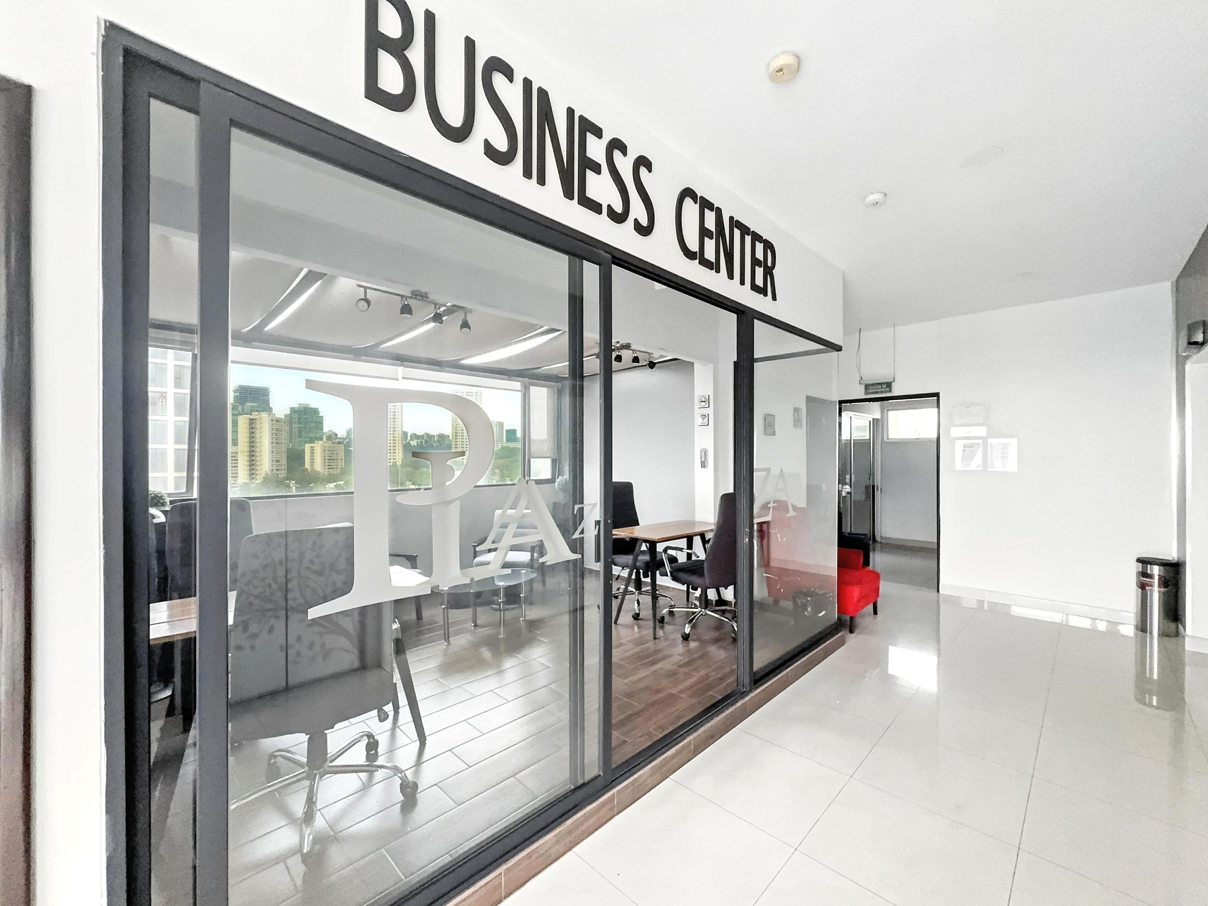Een business center met een grote glazen deur, moderne bureaustoelen en een uitzicht op de stad door de ramen.