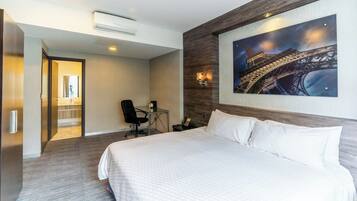 Habitación de hotel con una cama grande, un escritorio con una silla, un cuadro de la Torre Eiffel y un equipo de aire acondicionado.