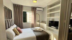 Ein modernes Schlafzimmer mit einem Bett, einem Fernseher auf einem Regal und einer Klimaanlage.
