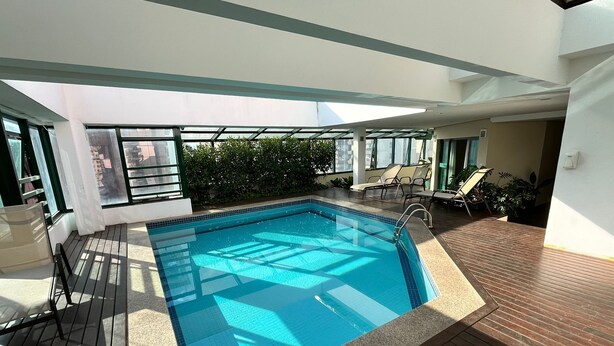 Ein Poolbereich auf dem Dach mit klarem, blauem Pool, einer Holzterrasse und Liegestühlen.