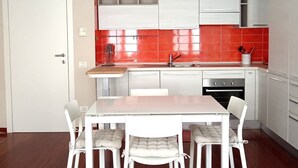 A modern kitchen with white cabinets, a red backsplash, and a dining area with white chairs and a table. - Lovely Flat - Magolfa 21 (Milan)