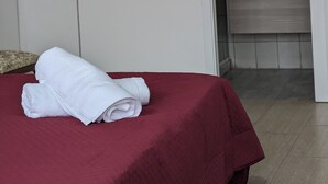 A neatly made bed with a red bedspread and white towels, a wooden floor, and a bathroom with a modern sink and mirror. - CAPORELLA Dimora della via Appia (Potenza)