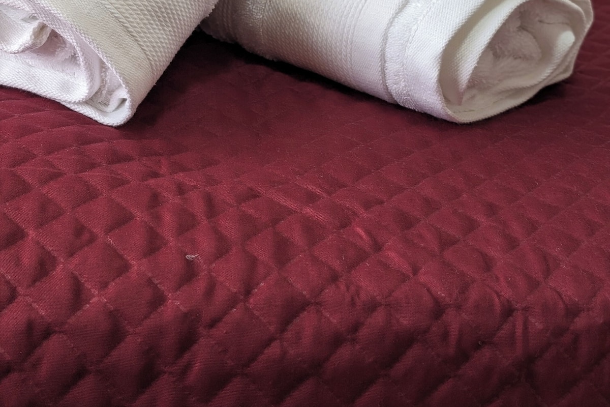 Two rolled white towels on a red quilted bedspread.
