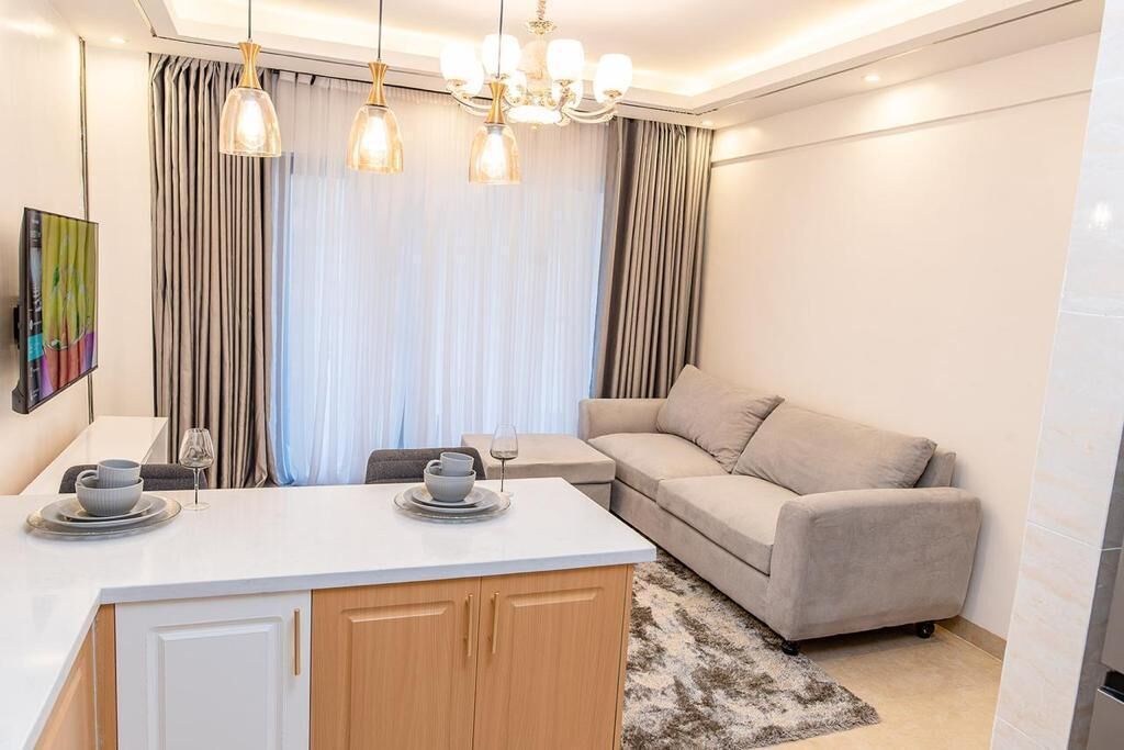 A modern living room with a sofa, a small table, and a kitchen area with a counter and cabinets.