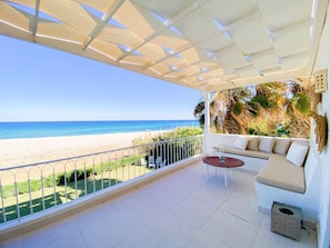 Un balcon avec vue sur la plage, un canapé blanc, une petite table et une poubelle.