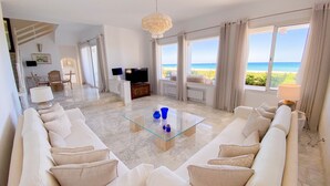 A spacious living room with a large sofa, a glass coffee table, and a television. The room has large windows with a view of the ocean. - The Luxury Sea House in Hammamet (Hammamet)