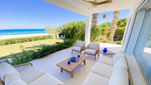 A sunlit patio with a view of the beach, wicker furniture, and a ceiling fan. - The Luxury Sea House in Hammamet (Hammamet)