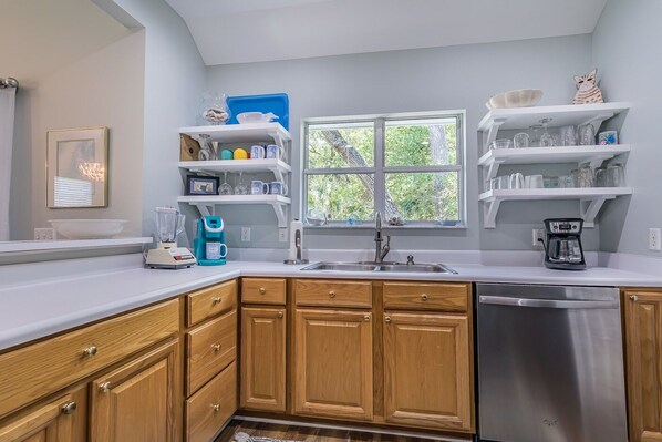 A modern kitchen with wooden cabinets, a stainless steel dishwasher, and a window providing natural light.