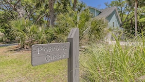 A wooden sign with the text "Porpoise Circle" in a natural setting with palm trees and a house in the background. - Golf cart included, amenity cards available, pet friendly - great for young families, 601 Porpoise Circle (Fripp Island)