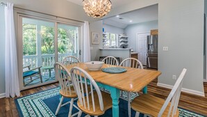 A dining area with a wooden table and white chairs, a chandelier, and a view through a glass door to an outdoor deck. - Golf cart included, amenity cards available, pet friendly - great for young families, 601 Porpoise Circle (Fripp Island)
