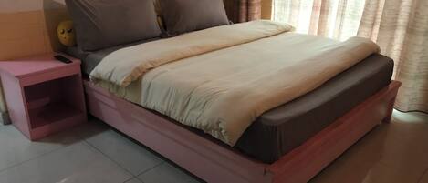 A bed with a wooden frame, a pink nightstand, and a small shelf.