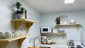 Une cuisine compacte avec des étagères en bois, un four à micro-ondes, une bouilloire et une cuisinière.