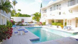 Une piscine avec des chaises longues et un bâtiment blanc doté de balcons.