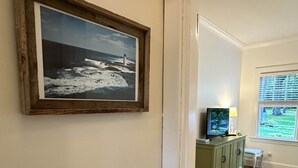 A hallway with a framed photograph on the wall, a wooden floor, a green cabinet, a television, and a window with a view of greenery. - Arden Cottage (Mount Vernon)