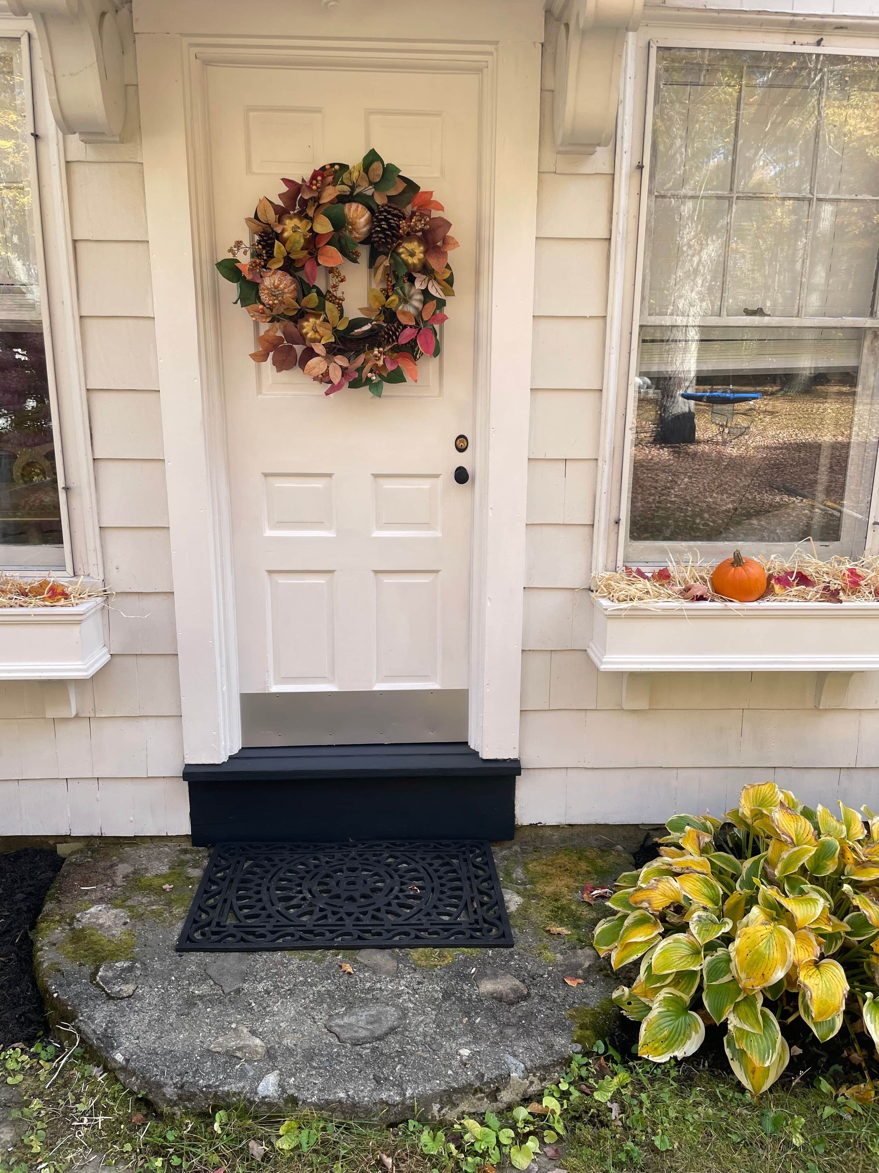 A white front door with a wreath, a black doormat, and a stone step leading to the door.