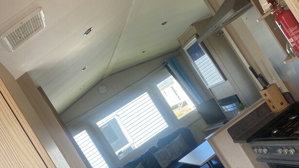 A compact kitchen with a stove, sink, and a dining area with a blue sofa. - Coastal Cabin Retreat in Rhyl (Rhyl)