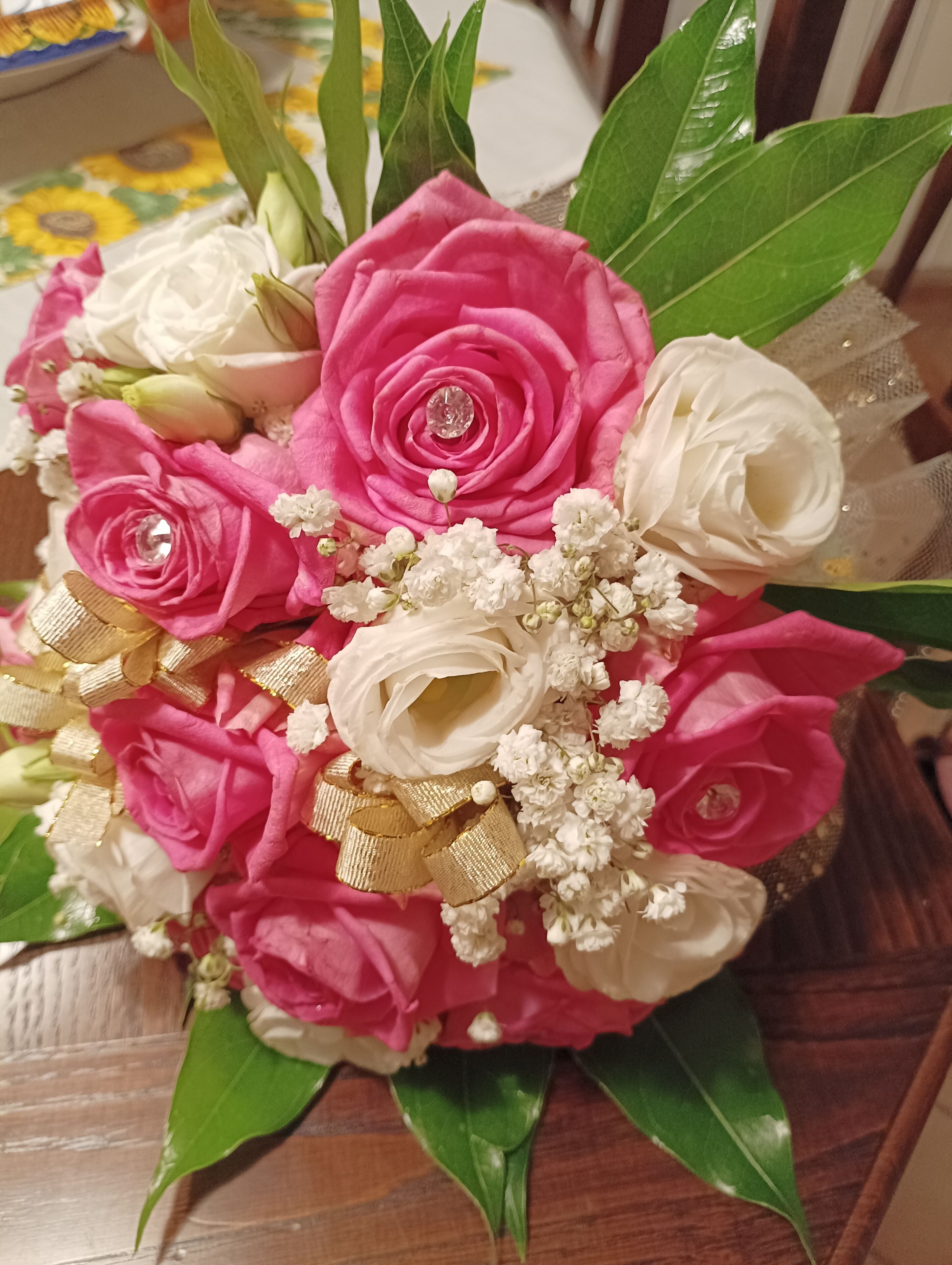Un ramo de rosas rosadas y blancas con cintas doradas y una gema transparente, sobre una superficie de madera.