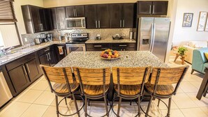 Una cocina moderna con armarios oscuros, encimeras de granito, un refrigerador de acero inoxidable y una isla central con taburetes de bar.