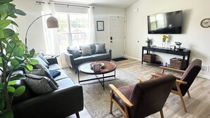A modern living room with a sofa, armchairs, a coffee table, and a TV on a stand.