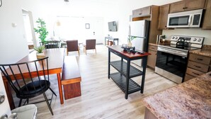 A modern kitchen with a dining area, wooden cabinets, a microwave, stove, and a ceiling fan.