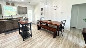 A modern kitchen with a wooden dining table, a bench, and a black metal shelf.