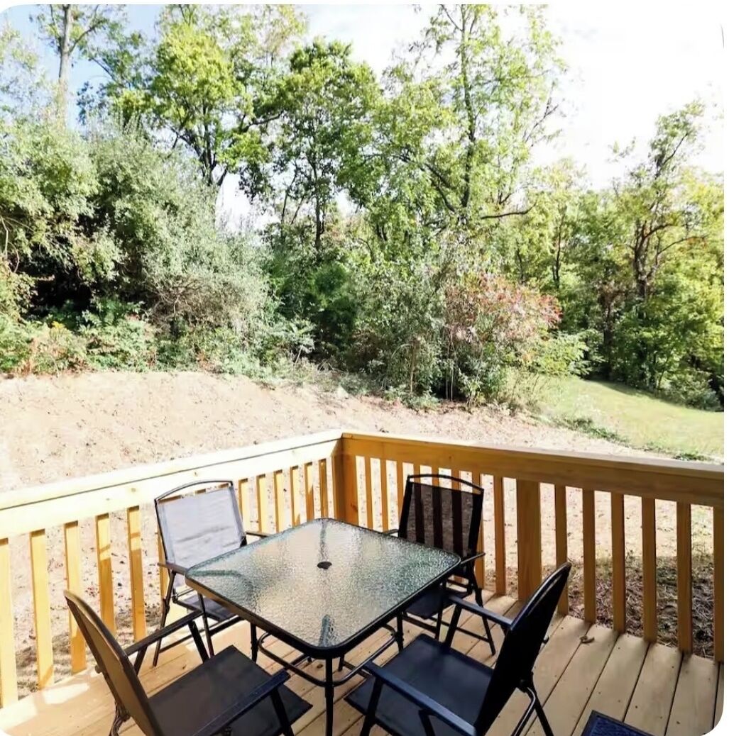 Eine Terrasse mit Glastisch und Stühlen, umgeben von Bäumen und einem Feldweg.