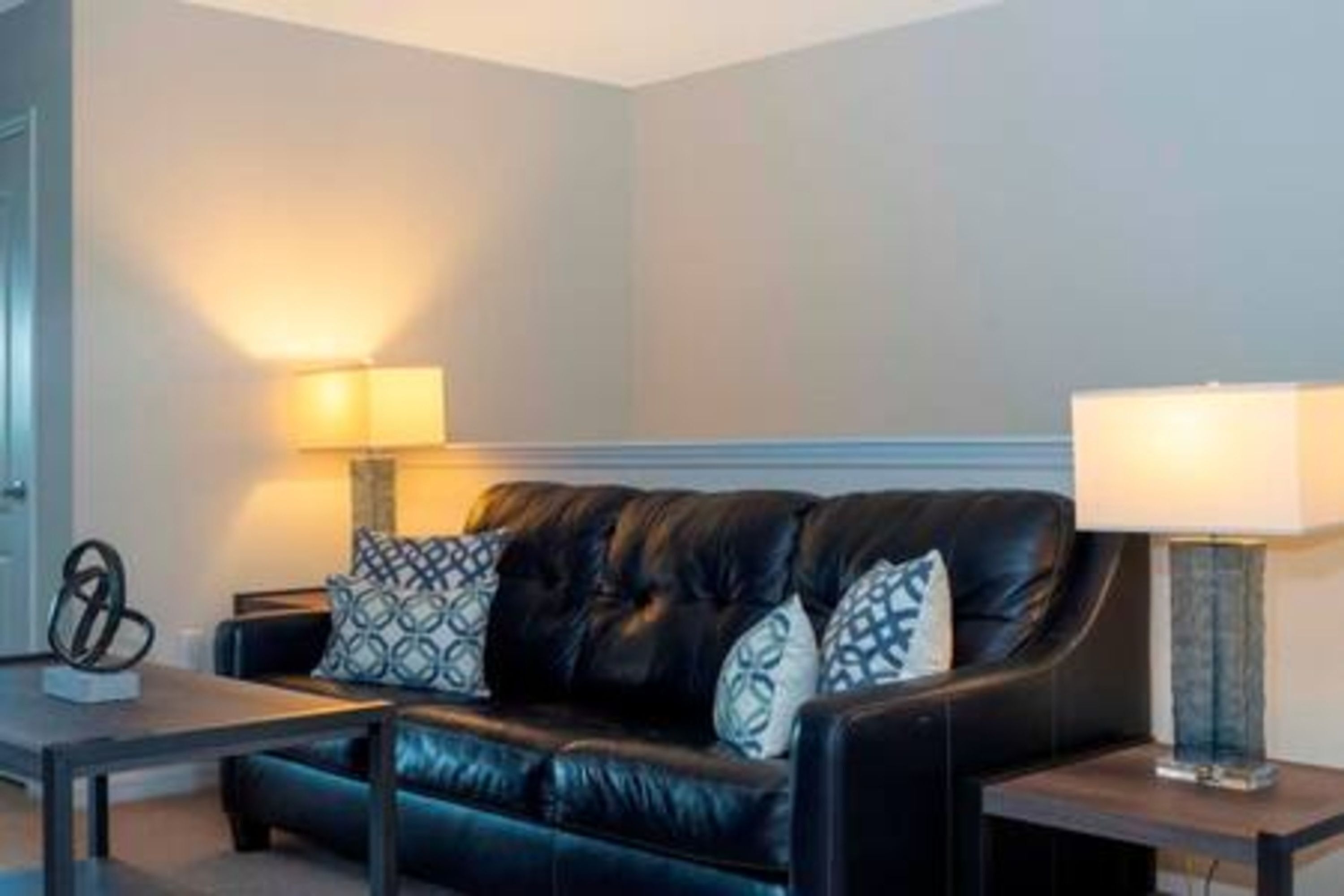 A modern living room with a black leather sofa, patterned cushions, a side table, and two wall-mounted lamps.