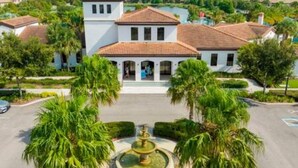 A white building with a red-tiled roof, surrounded by palm trees and a fountain. - Free Water Park Private Pool and Lakeview (Kissimmee)