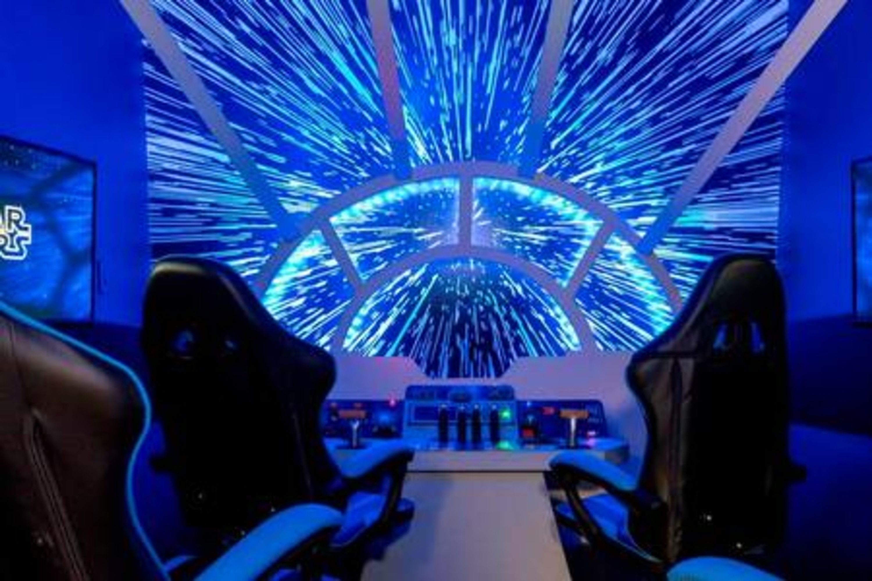 A gaming room with two gaming chairs, a control panel, and a large LED screen displaying a dynamic blue pattern.