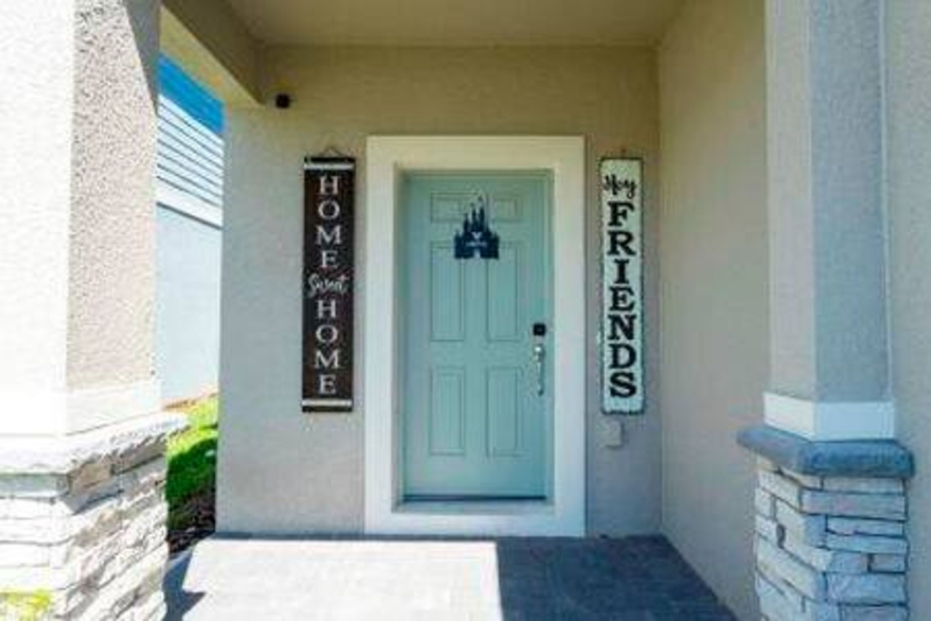 La entrada de una casa con una puerta azul claro, un letrero que dice 'HOME' y un letrero que dice 'FRIENDS'.