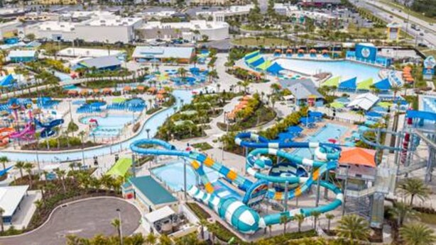 Parque aquático com várias piscinas e toboáguas, cercado por edifícios e palmeiras.