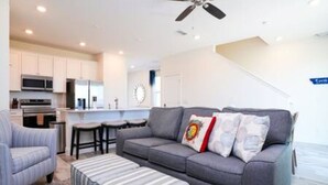 Uma sala de estar moderna com um sofá cinzento, um banquinho riscado e um ventilador de teto.