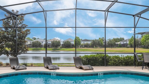 A swimming pool with lounge chairs, a covered area, and a view of houses and a lake. - 5 Suites - Game Room Theater Room Private Pool (Kissimmee)