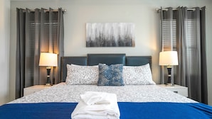 A neatly made bed with a blue blanket and white towels, two bedside lamps, and a wall-mounted abstract painting. - 5 Suites - Game Room Theater Room Private Pool (Kissimmee)