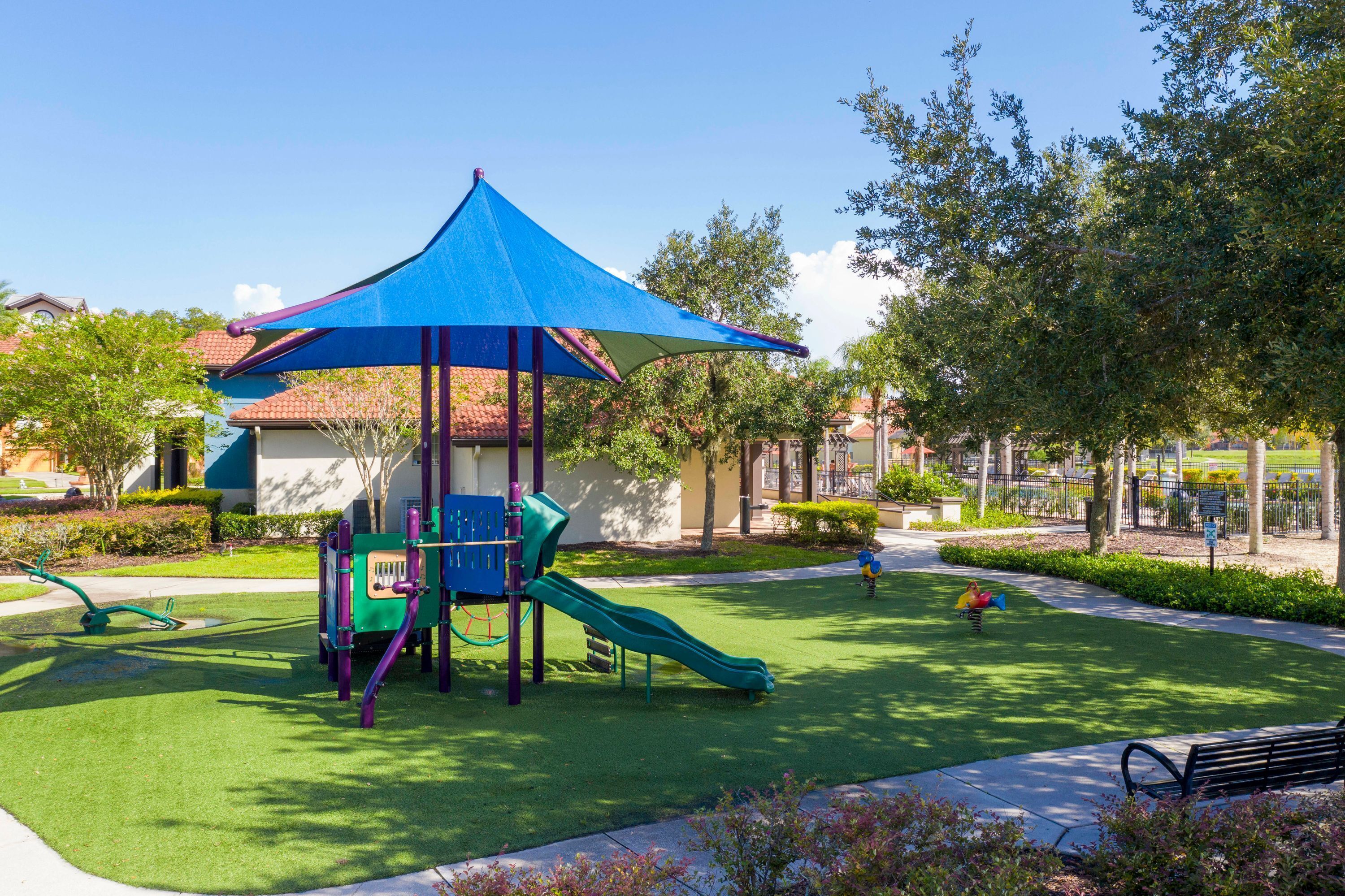 Un parque infantil con tobogán y estructuras para escalar, rodeado de césped cuidado y árboles.