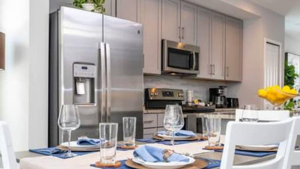 A modern kitchen with stainless steel appliances, a dining table set for four, and a microwave above it. - Beautiful 4 Bed 3 5 Bath With Jacuzzi (Kissimmee)