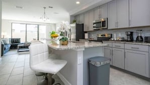 A modern kitchen with grey cabinets, a central island, and a seating area with a white chair. - Beautiful 4 Bed 3 5 Bath With Jacuzzi (Kissimmee)