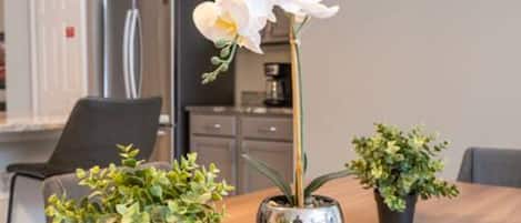 A dining table with a potted orchid, a potted fern, and a small plant.