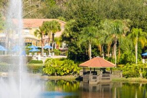 A tranquil pond with a fountain, surrounded by lush greenery and a gazebo. - Cozy 3 BR w Private Pool (Kissimmee)