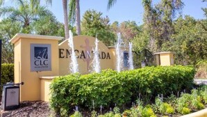 A sign for "EMANCIPADA" with a logo, surrounded by lush greenery and a water feature. - Cozy 3 BR w Private Pool (Kissimmee)