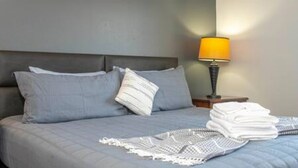 A neatly made bed with a grey duvet, a white throw blanket, and a folded white towel. - Cozy 3 BR w Private Pool (Kissimmee)