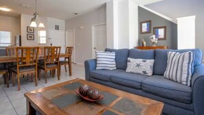 A living room with a blue sofa, wooden dining table, and chairs. - Cozy 3 BR w Private Pool (Kissimmee)