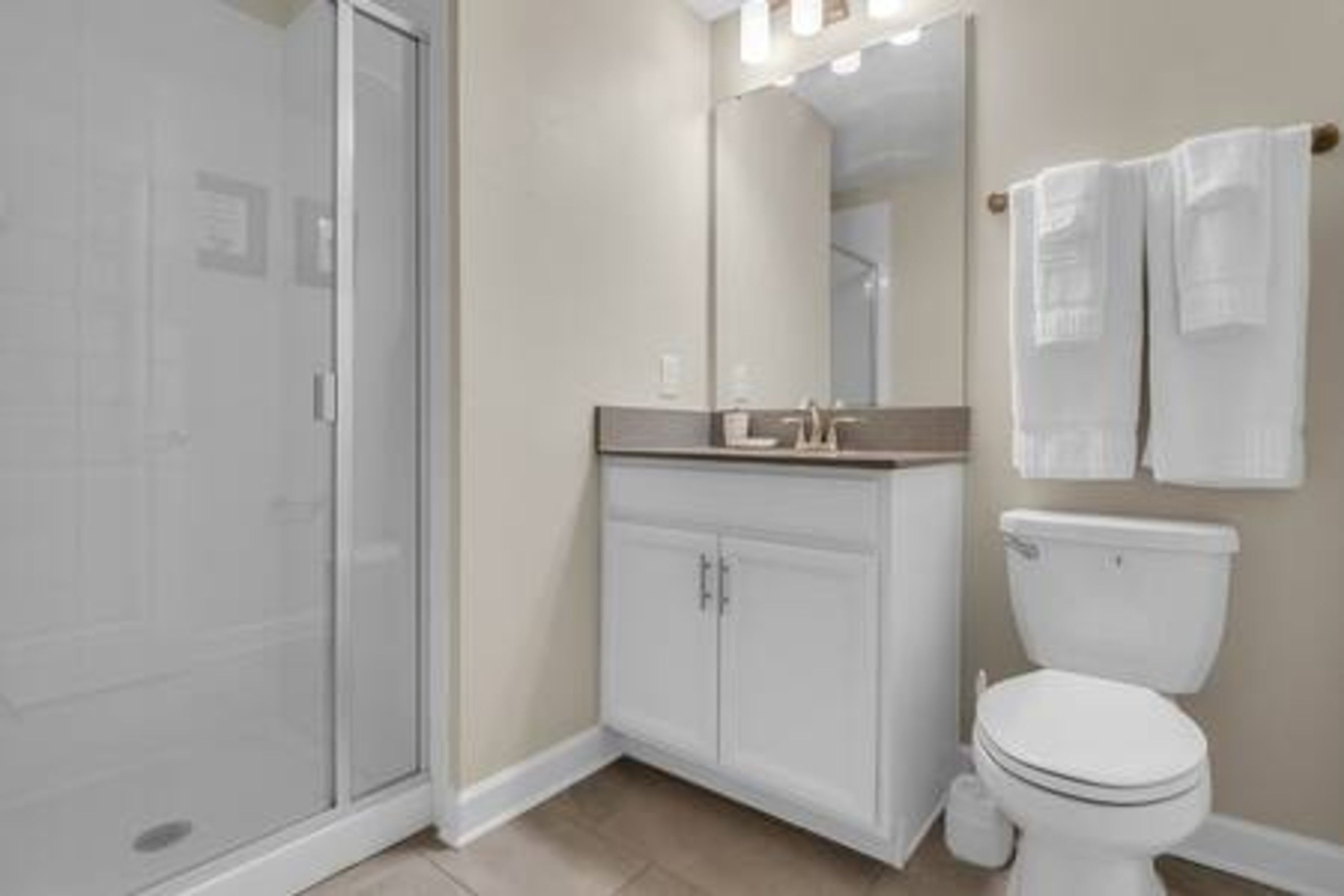 A modern bathroom with a glass shower enclosure, a white vanity with a mirror, and a toilet.