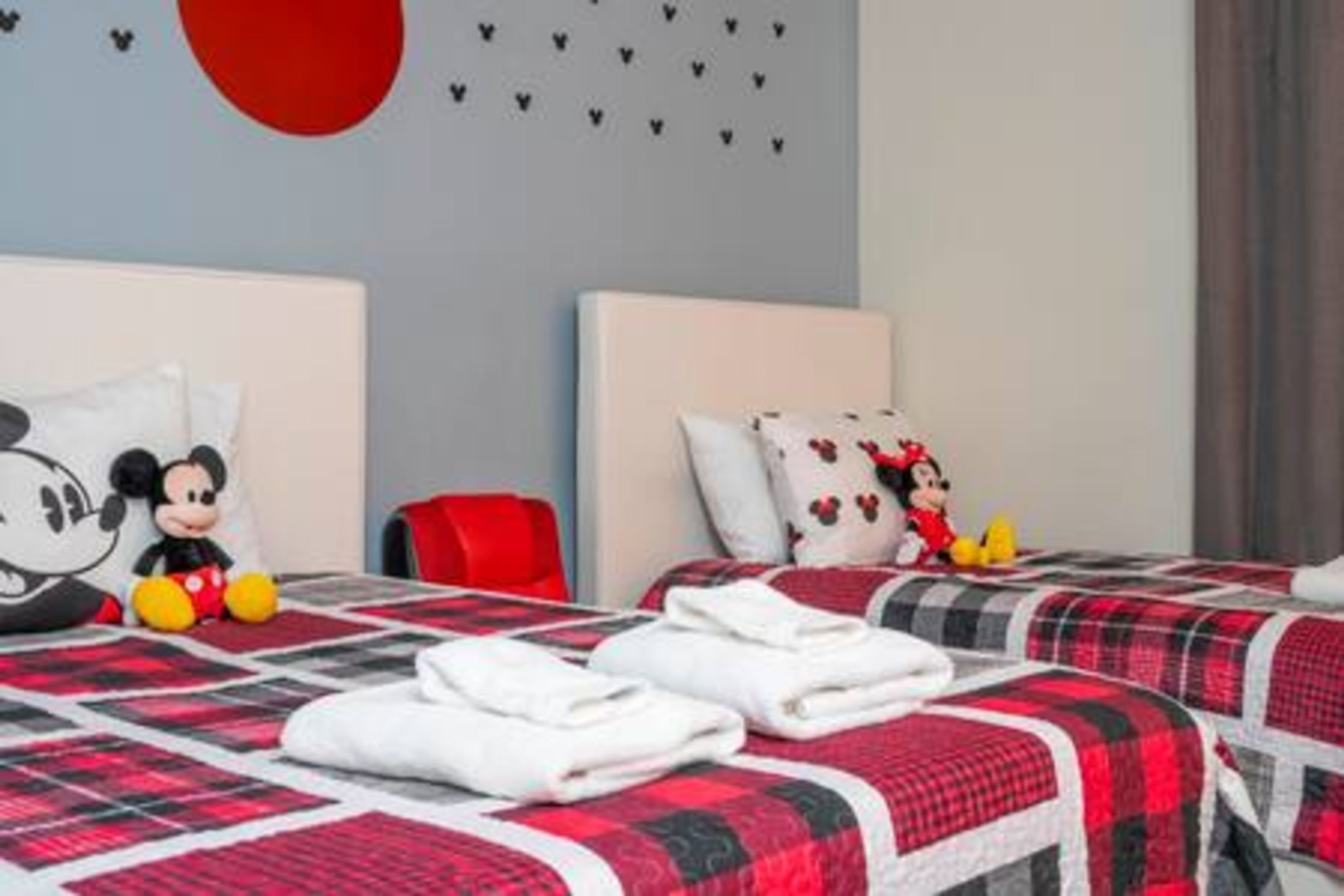 A hotel room with two beds, each with a red and black checkered bedspread, white pillows, and Mickey Mouse plush toys.