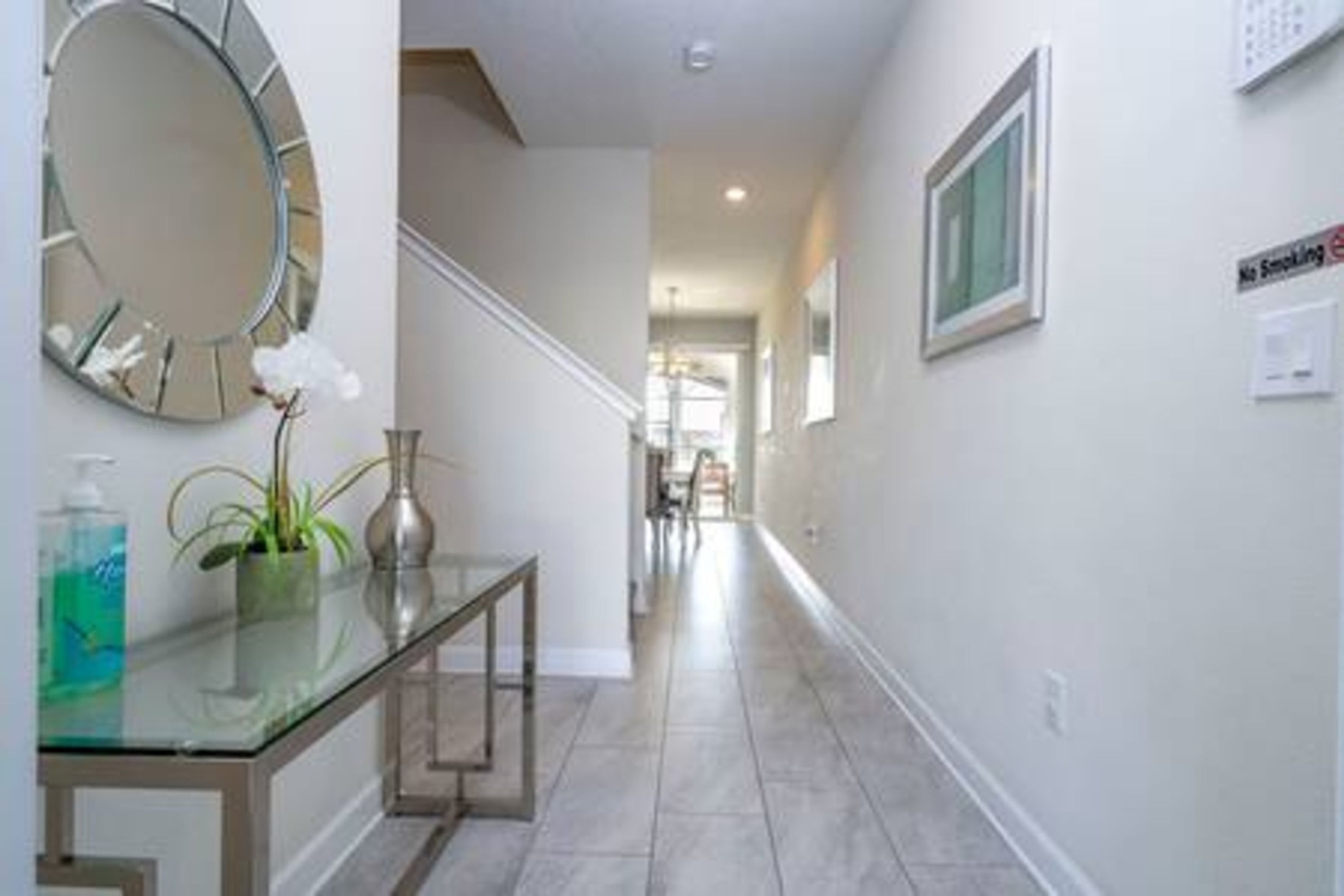 A hallway with a glass-top table, a round mirror, and a 'No Smoking' sign.