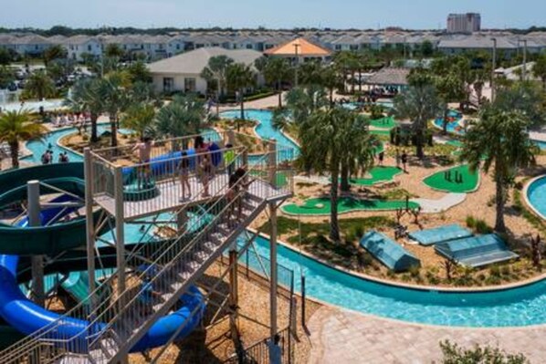 A water park with multiple slides and pools, surrounded by palm trees and a residential area in the background.