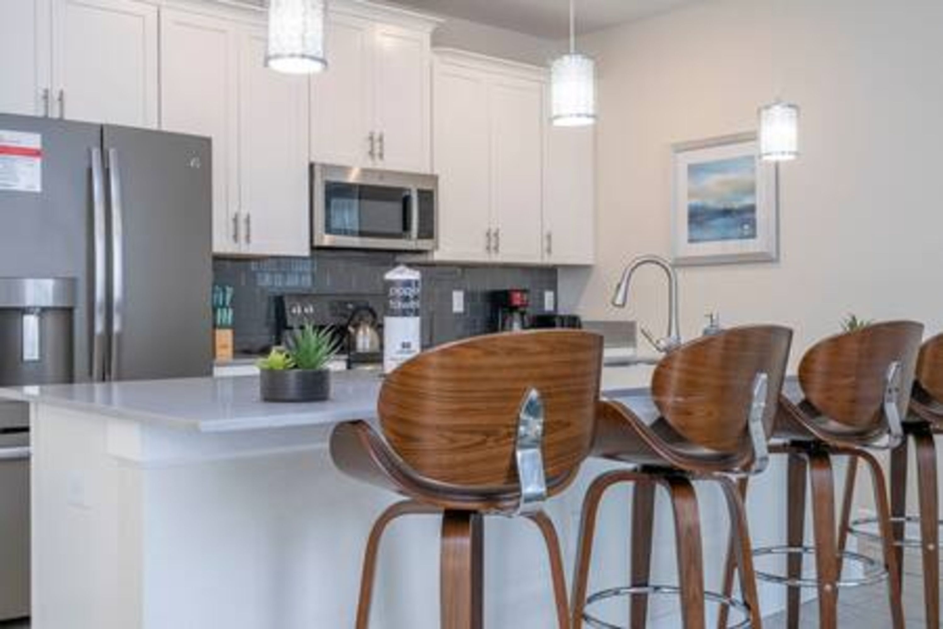 A modern kitchen with white cabinets, stainless steel appliances, and wooden bar stools.