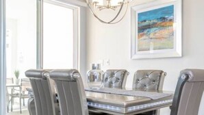 A dining area with a glass-top table, cushioned chairs, and a chandelier. - Gorgeous Home With Pool and Lake View (Kissimmee)