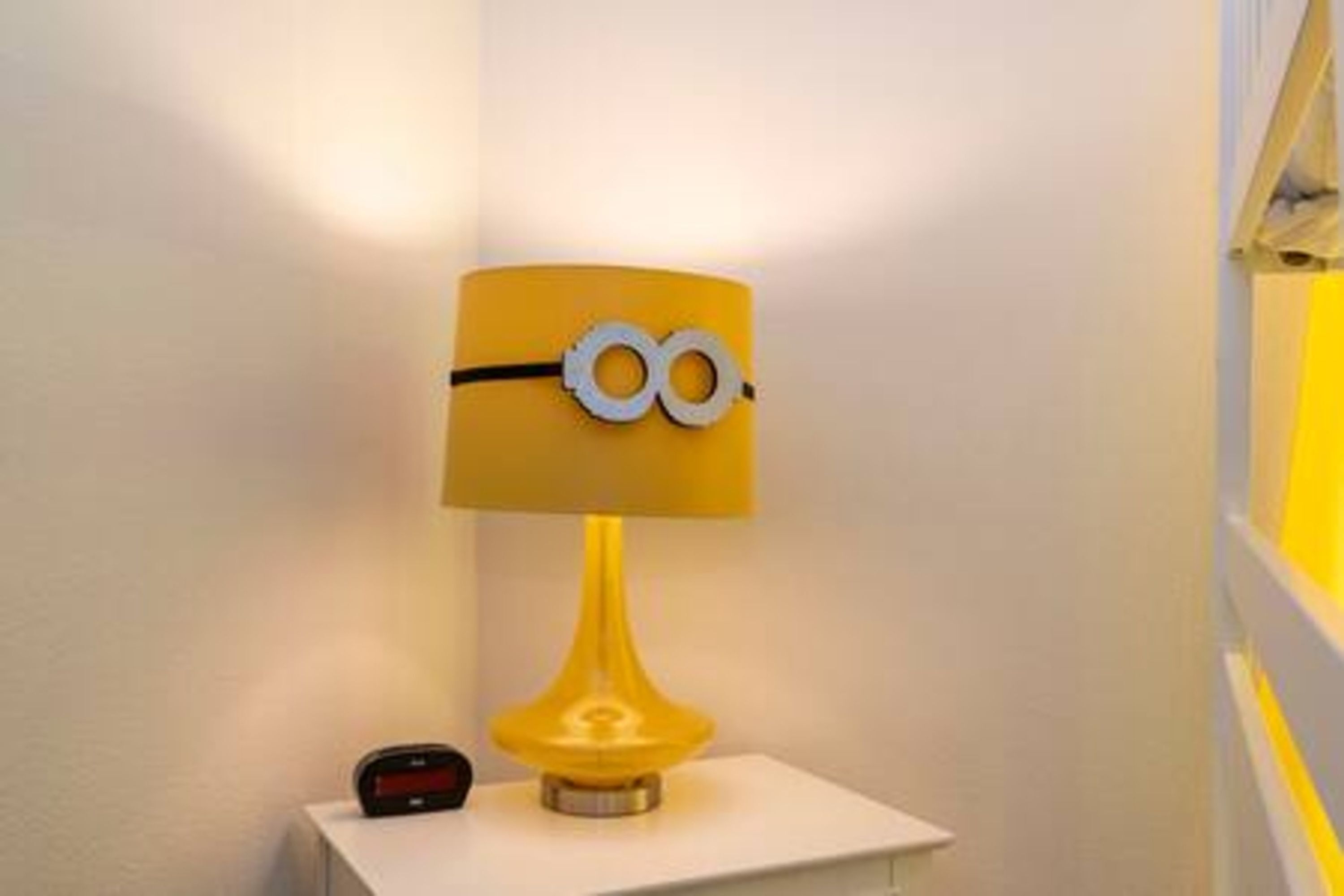 A yellow lamp with a Minion design on the lampshade, placed on a white surface.