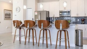 A modern kitchen with white cabinets, stainless steel appliances, and three wooden bar stools. - Gorgeous Home With Pool and Lake View (Kissimmee)